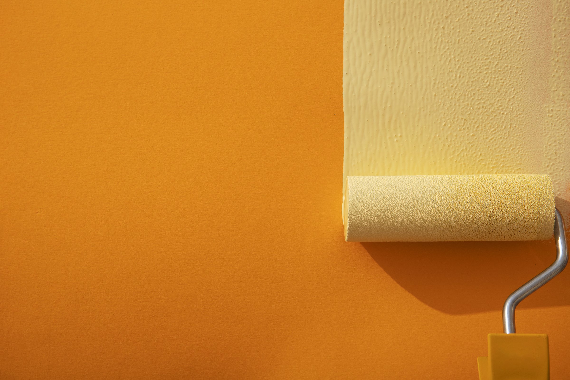 Paint roller applying a fresh cream coat over an orange wall